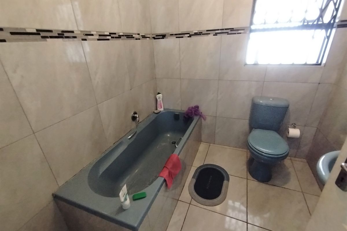 A functional bathroom featuring tiled walls and flooring, equipped with a bathtub and toilet, with security bars installed on the window.