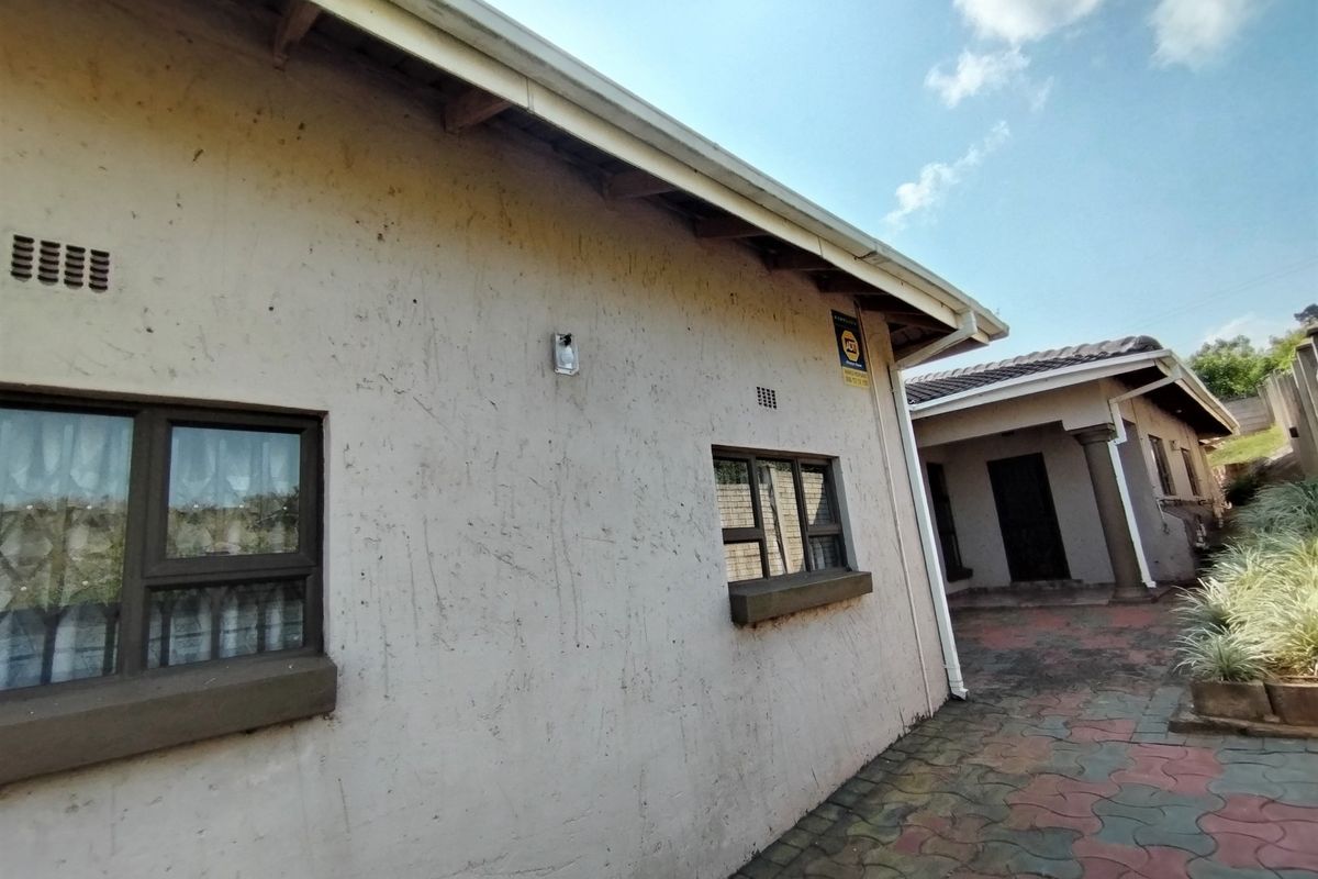 Rear exterior view of the property featuring a paved courtyard area, aluminium window frames, and external wall finishes requiring maintenance.