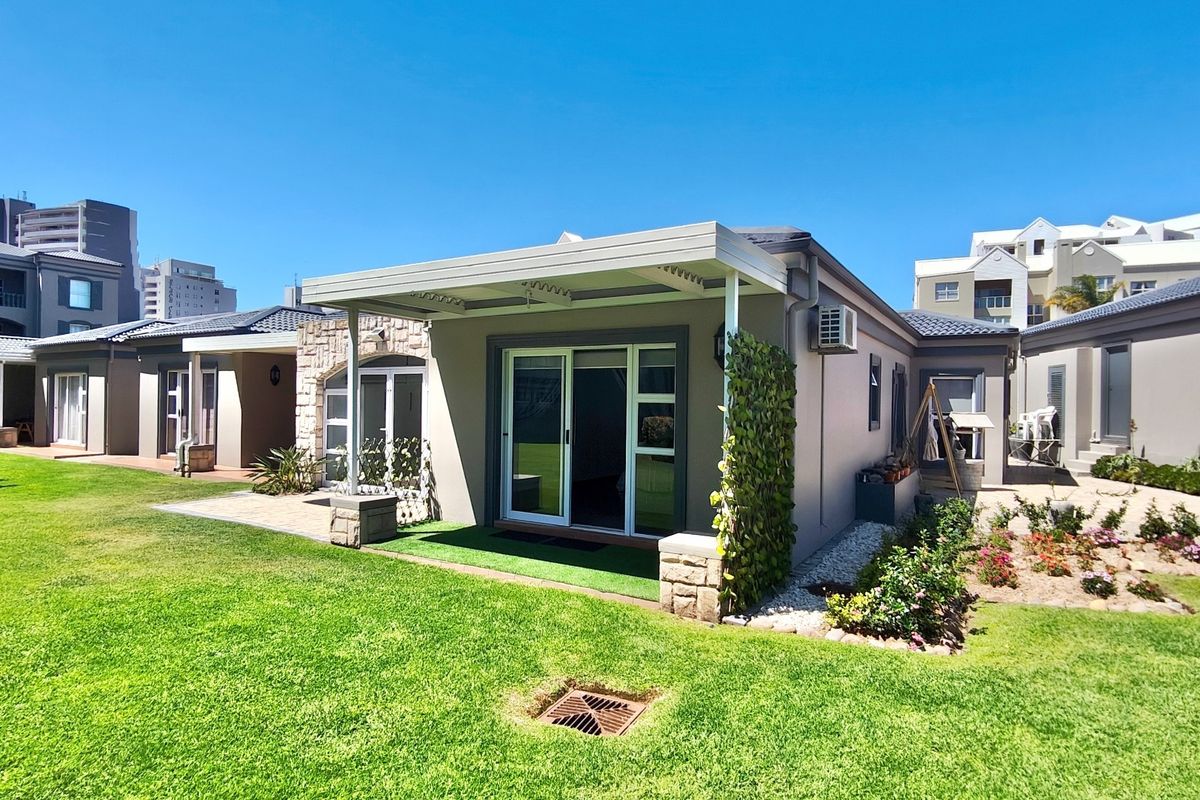 Rear view of the property featuring a covered patio, sliding glass doors, stone accents, and a well-maintained garden area.
