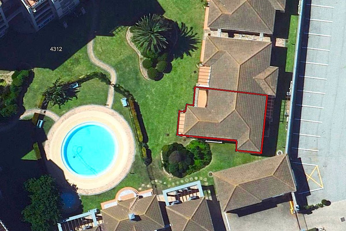Aerial view of the property showing the roof structure, surrounding landscaped garden, and communal swimming pool area.