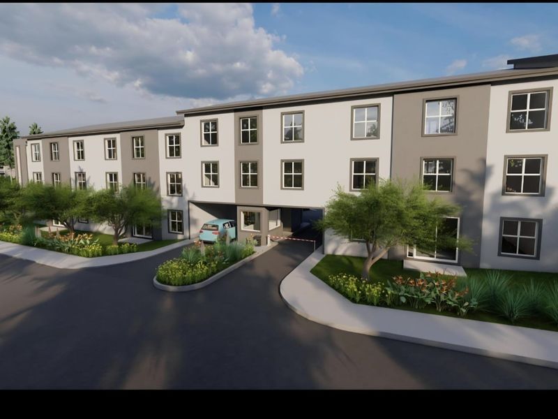 A modern multi-story retirement village building featuring a secure gated entrance, paved driveway, and well-maintained landscaped garden beds.