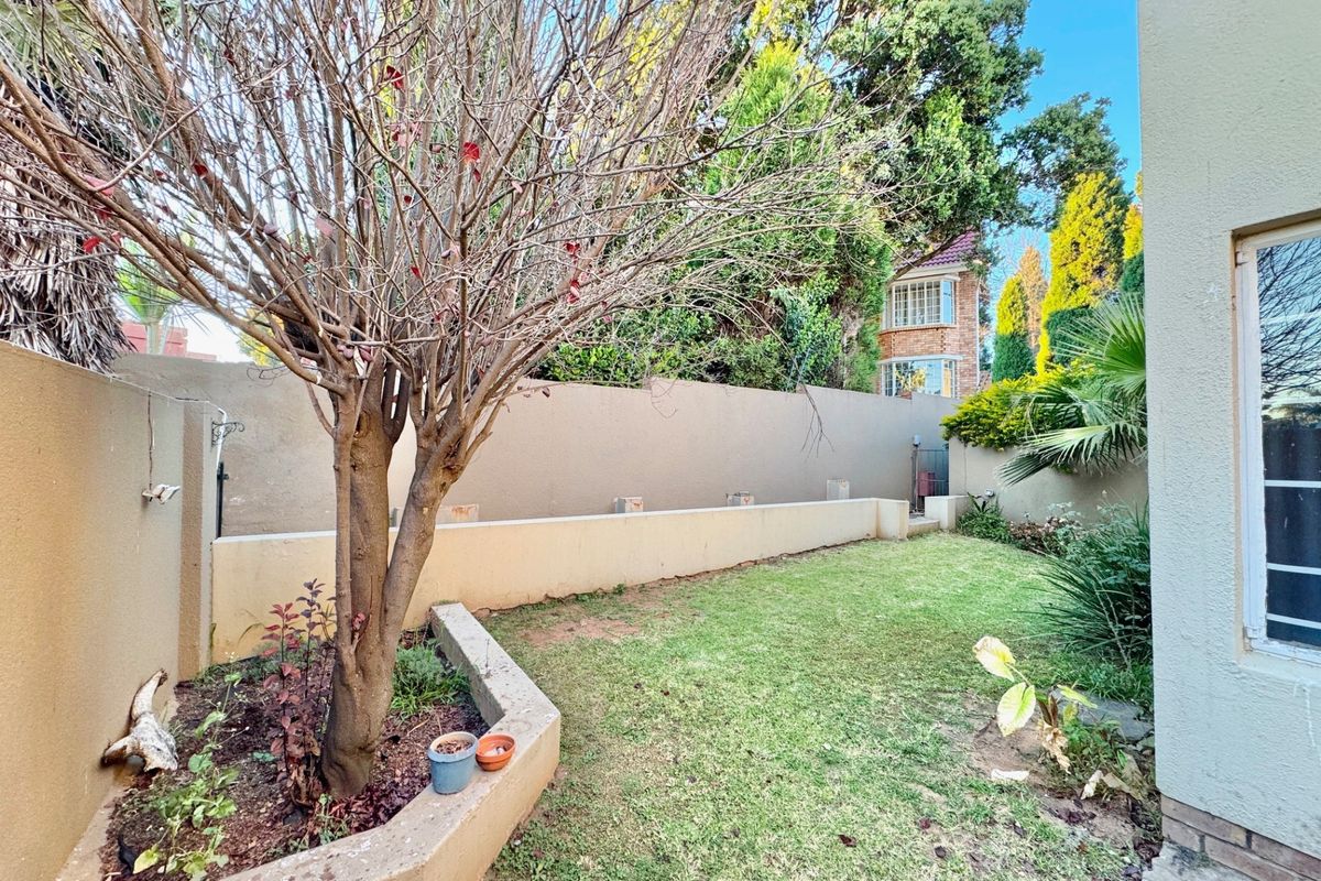 A private rear garden area featuring a lawn, established tree, and perimeter boundary walls, providing a quiet outdoor space.
