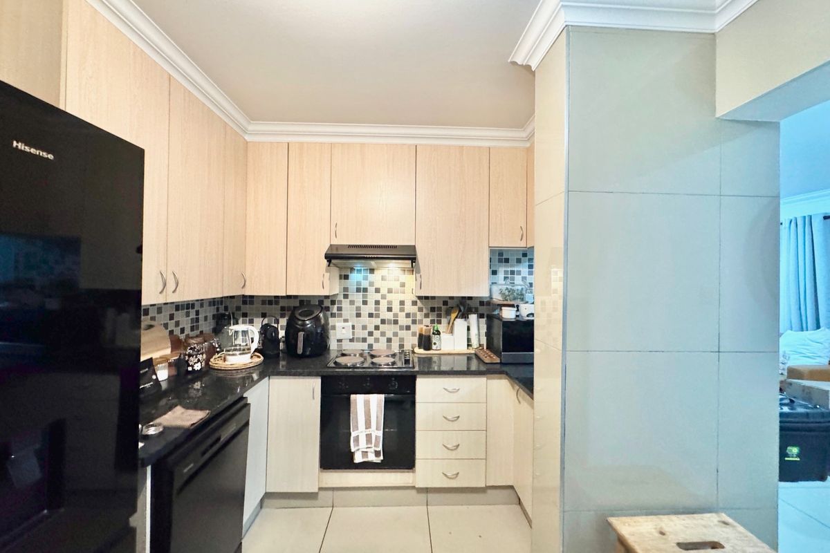 A functional kitchen featuring light wood cabinetry, dark granite countertops, a mosaic tile backsplash, and integrated appliances including an oven and extractor fan.