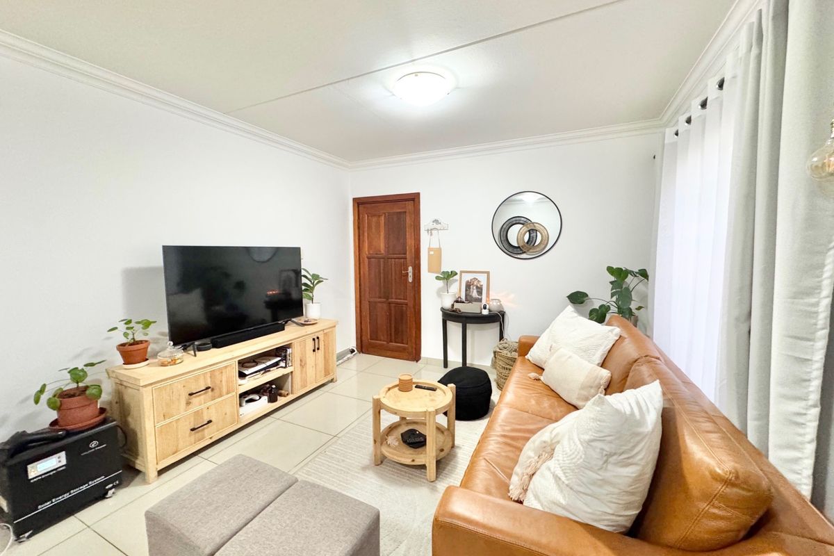 A bright and well-maintained living room featuring neutral tiled flooring, coved ceilings, and a solid timber door, offering a clean and functional living space.