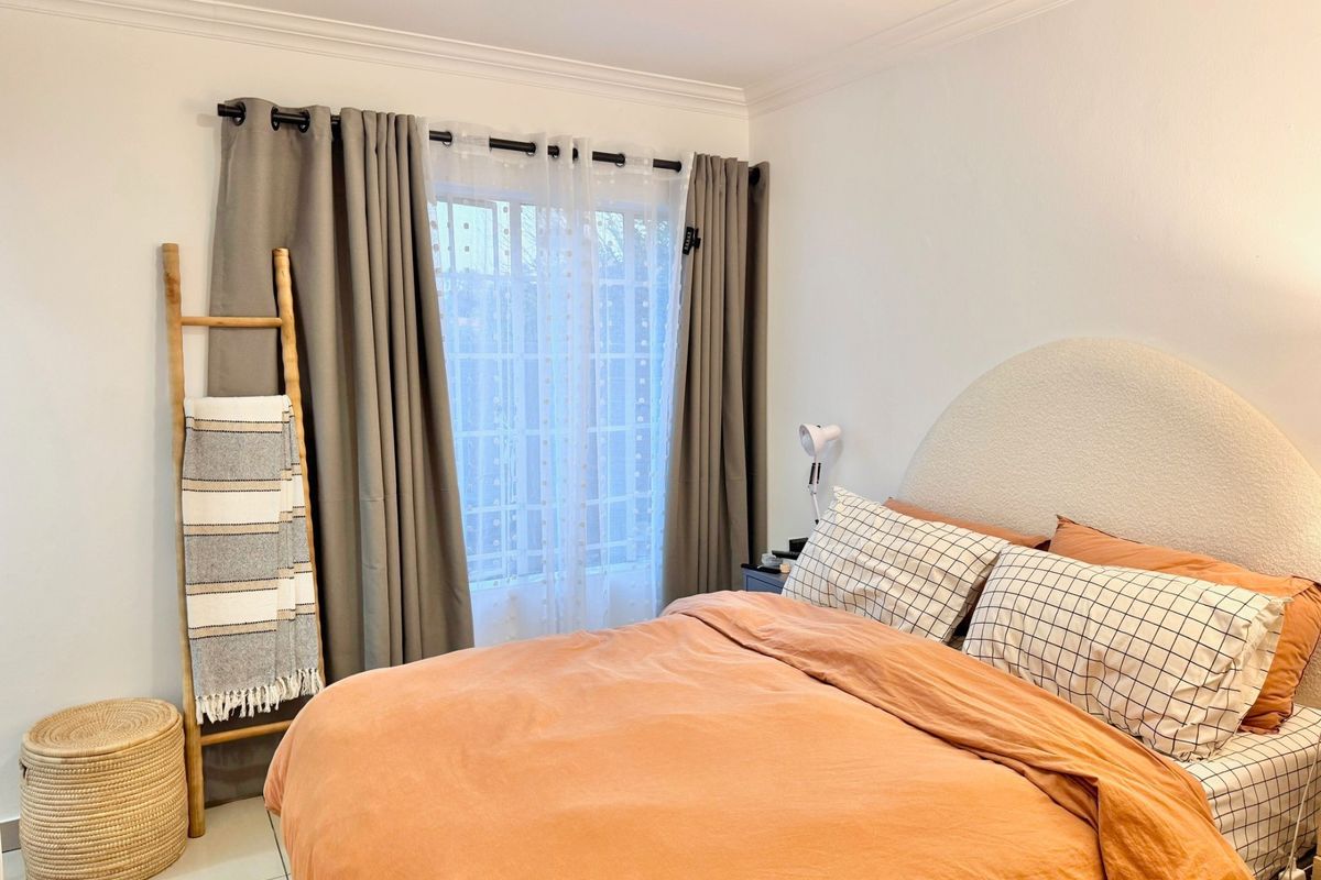A well-maintained bedroom featuring tiled flooring, decorative cornicing, and a window fitted with security bars, providing a bright and comfortable living space.