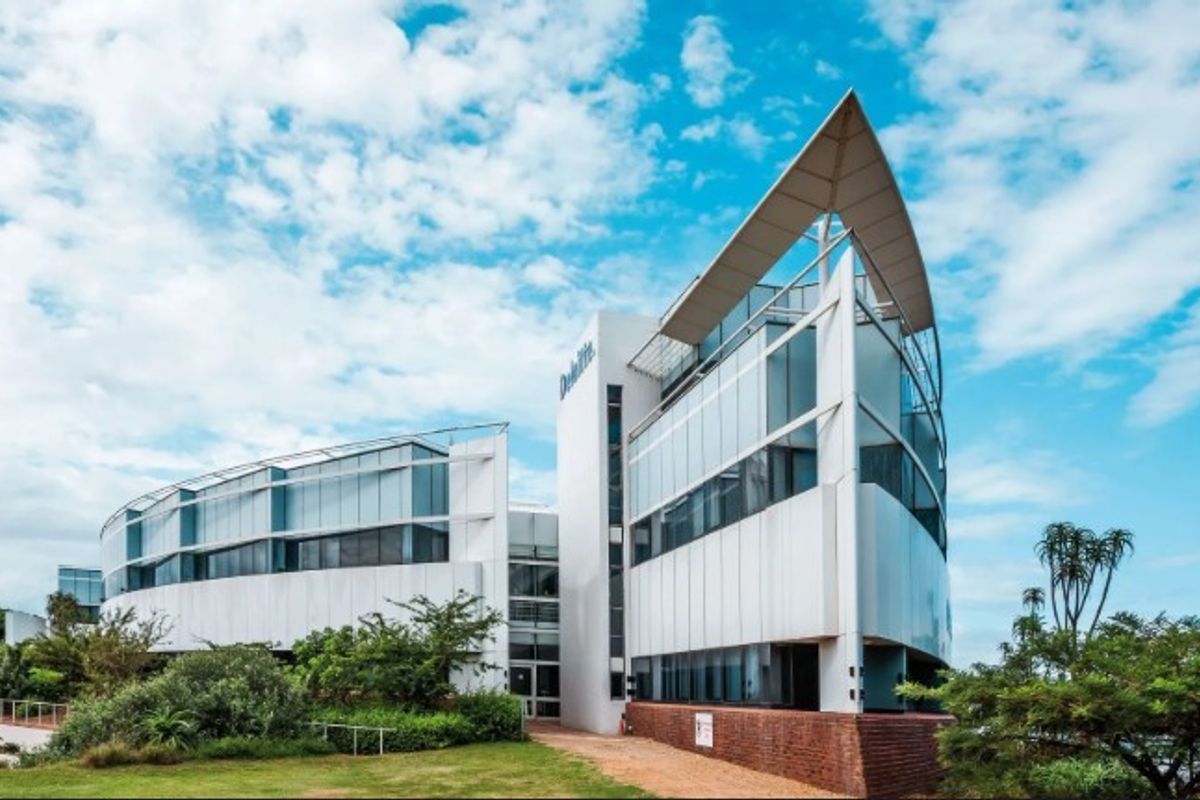 Modern multi-story office building featuring a striking curved glass facade, metal paneling, and a prominent architectural roof canopy set within landscaped grounds.
