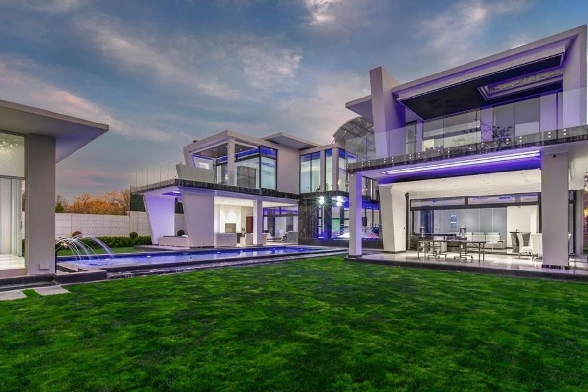 A modern luxury residence featuring a spacious rear garden, a swimming pool with water features, and expansive covered patio areas with contemporary architectural design.