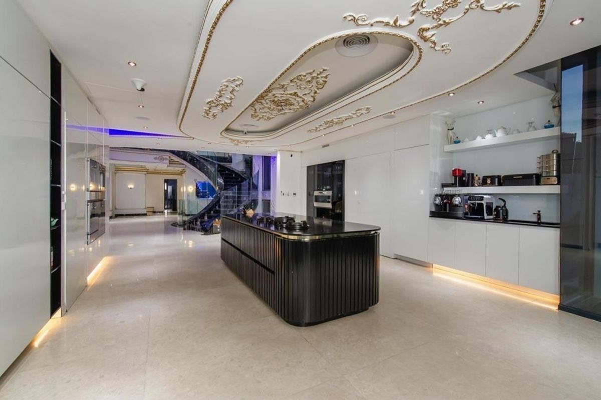 Modern luxury kitchen featuring a sleek black island, integrated appliances, high-gloss cabinetry, and ornate decorative ceiling detailing with ambient lighting.