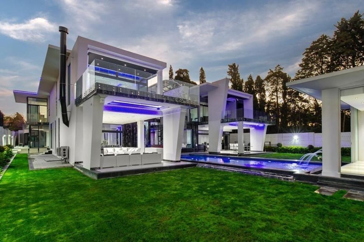 A stunning modern rear elevation featuring a sleek swimming pool, expansive covered patio areas, glass balustrades, and beautifully maintained garden landscaping.