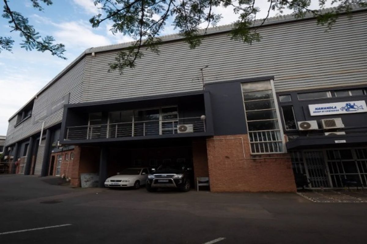 Front elevation of an industrial property featuring a combination of brick and corrugated metal cladding, with an integrated balcony and paved parking area.