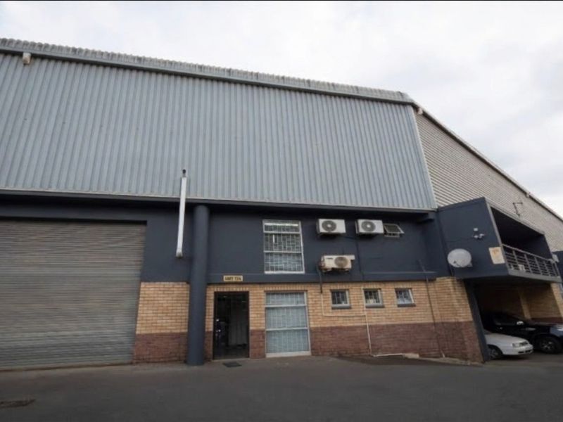 Industrial warehouse unit featuring a large roller shutter door, brick and metal cladding facade, and exterior air conditioning units.
