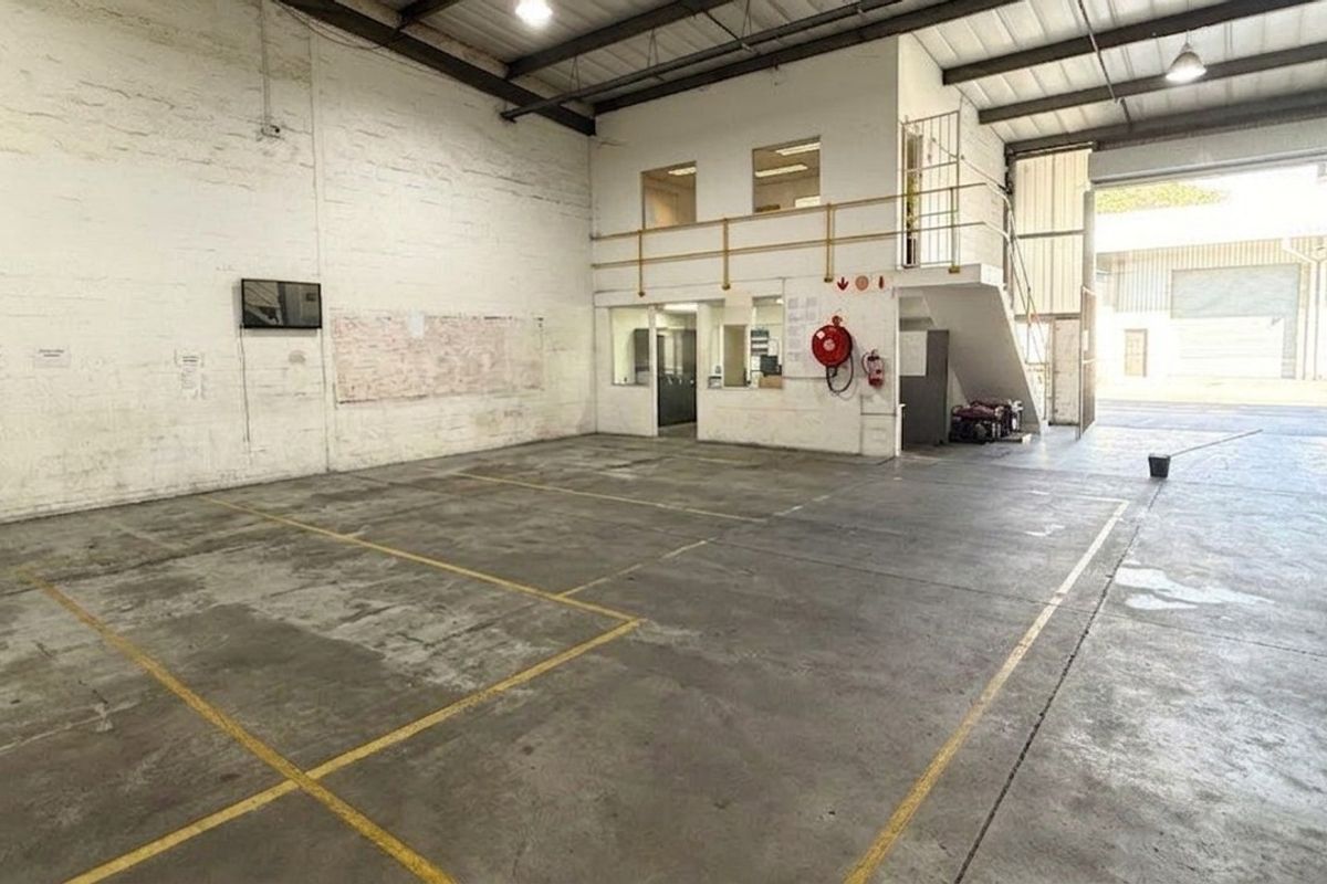 Spacious industrial warehouse unit featuring high ceilings with exposed trusses, a mezzanine level, concrete flooring, and a large roller shutter door for easy access.