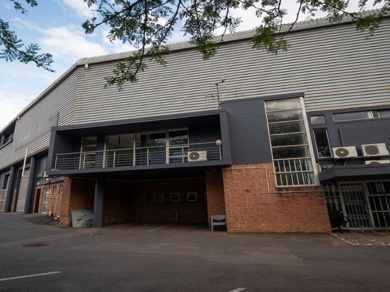 Industrial property exterior featuring a combination of brick and corrugated metal cladding, with an elevated balcony and paved driveway access.