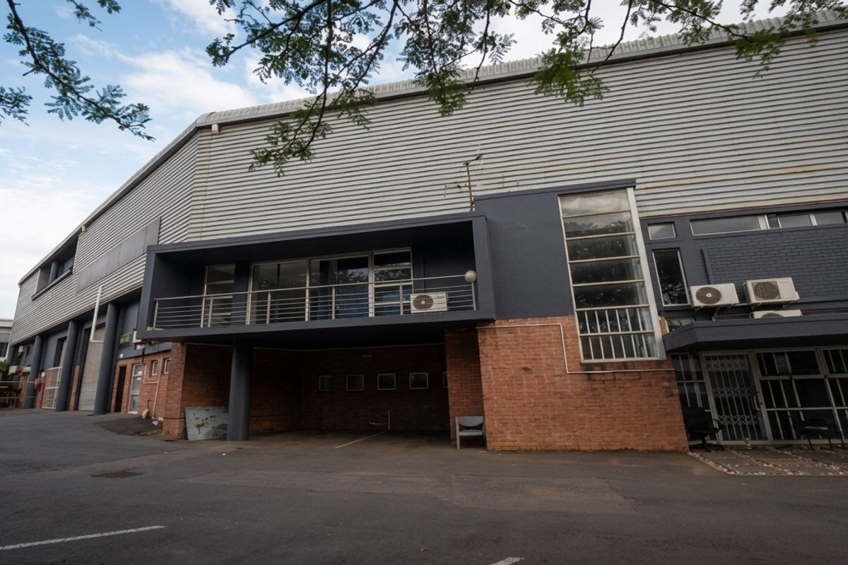 Industrial property exterior featuring a combination of brick and corrugated metal cladding, with an elevated balcony and paved driveway access.