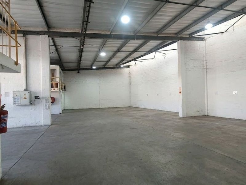 Spacious industrial warehouse unit featuring high ceilings with exposed steel trusses, concrete flooring, and integrated fire safety equipment.