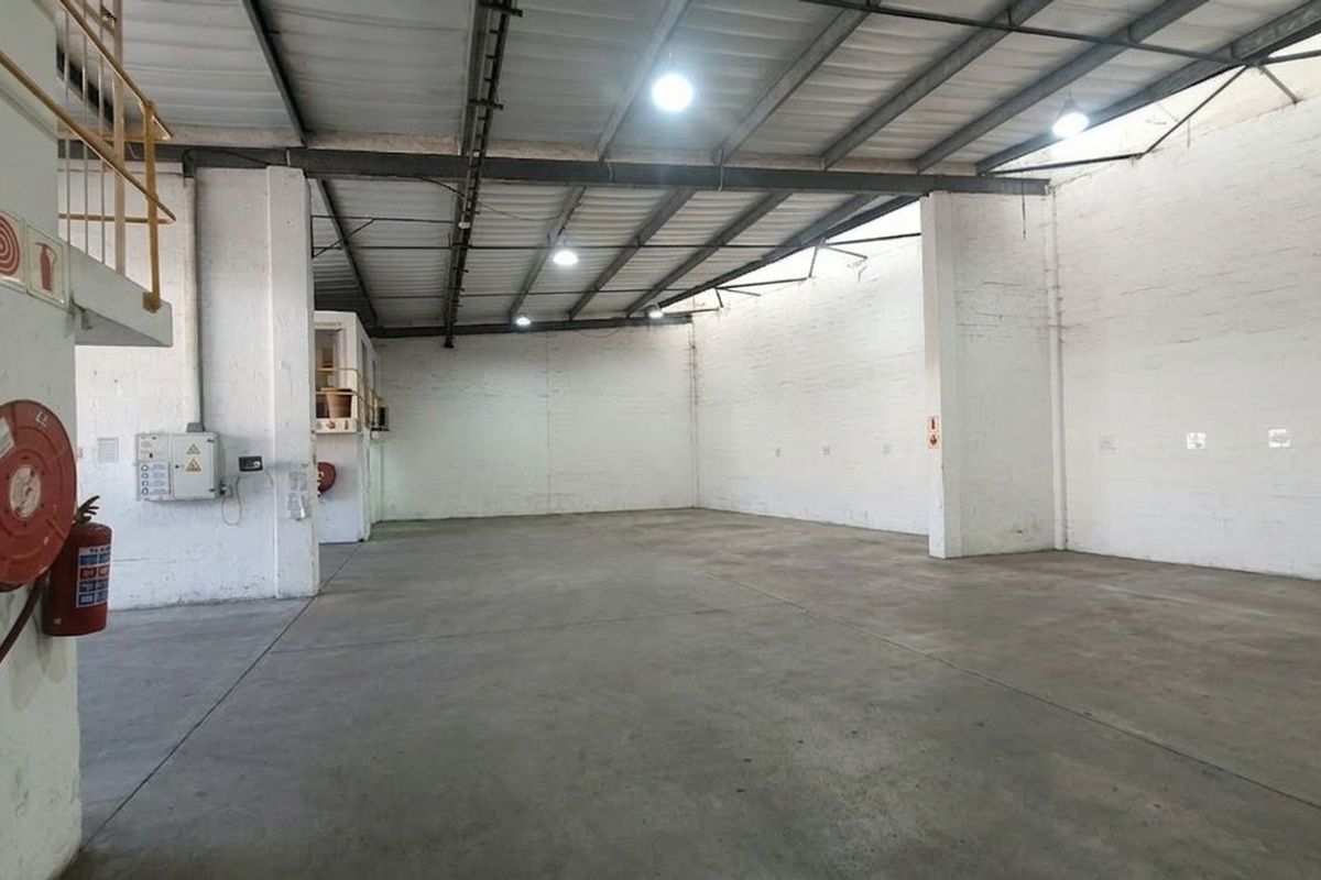 Spacious industrial warehouse unit featuring high ceilings with exposed steel trusses, concrete flooring, and integrated fire safety equipment.