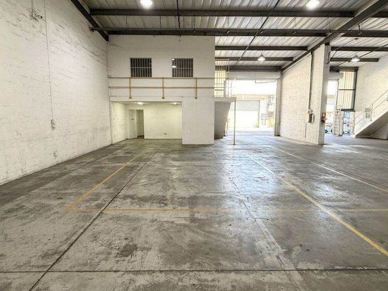 Spacious industrial warehouse unit featuring high ceilings with exposed steel trusses, concrete flooring, and a functional mezzanine level with staircase access.