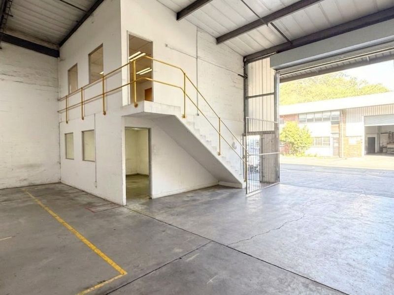 Spacious industrial warehouse unit featuring a concrete floor, mezzanine level with staircase, and a large roller shutter door for easy access.