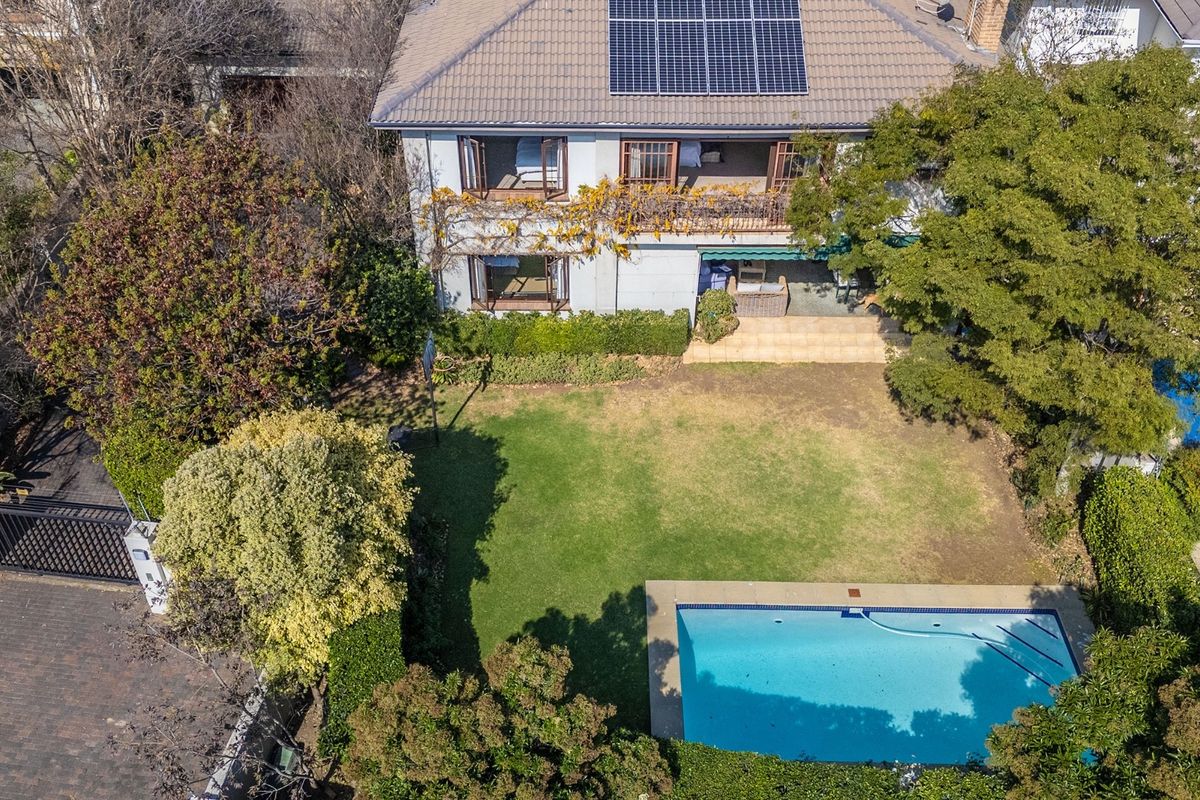 Aerial view of a residential property featuring a swimming pool, landscaped garden, paved patio, balcony, and roof-mounted solar panels.