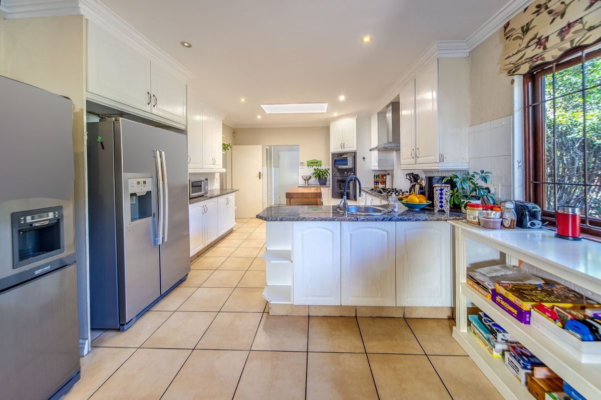 Spacious kitchen featuring white cabinetry, granite countertops, built-in oven, stainless steel extractor fan, and tiled flooring with natural light from a skylight.