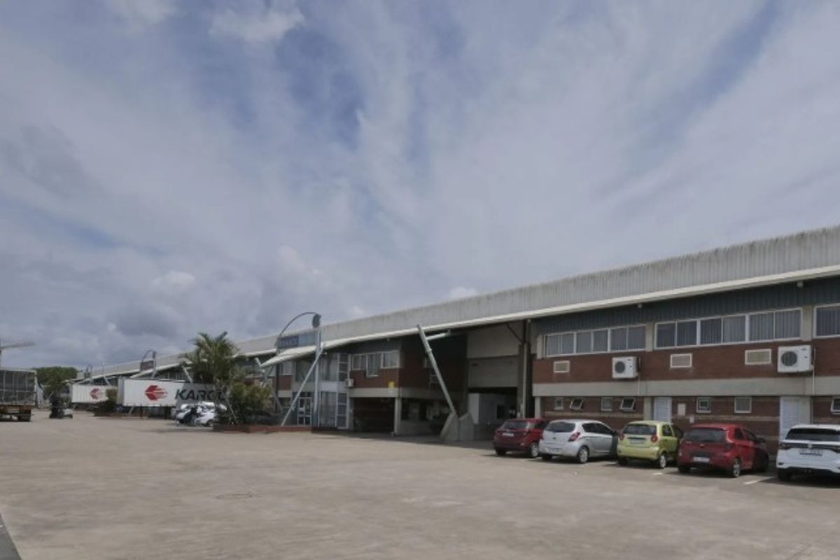 Wide-angle view of an industrial warehouse complex featuring a large concrete yard, brick facade, and multiple roller shutter access points.