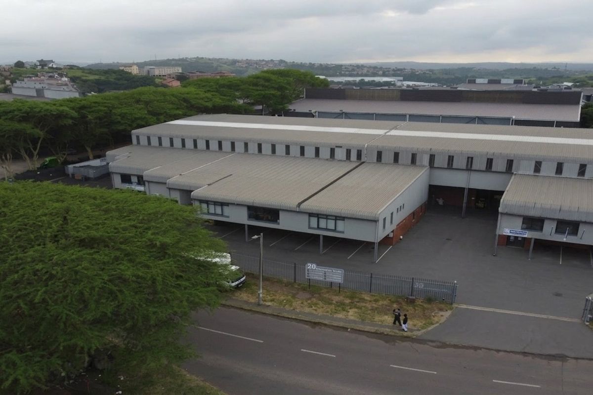 Aerial view of an industrial property featuring a large warehouse structure, covered loading bays, and an asphalt parking area with perimeter fencing.