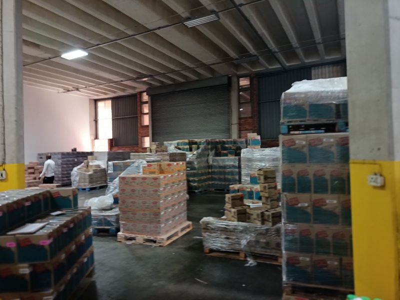 Spacious industrial warehouse area featuring high exposed concrete ceilings, durable flooring, and a large roller shutter door for efficient loading and access.