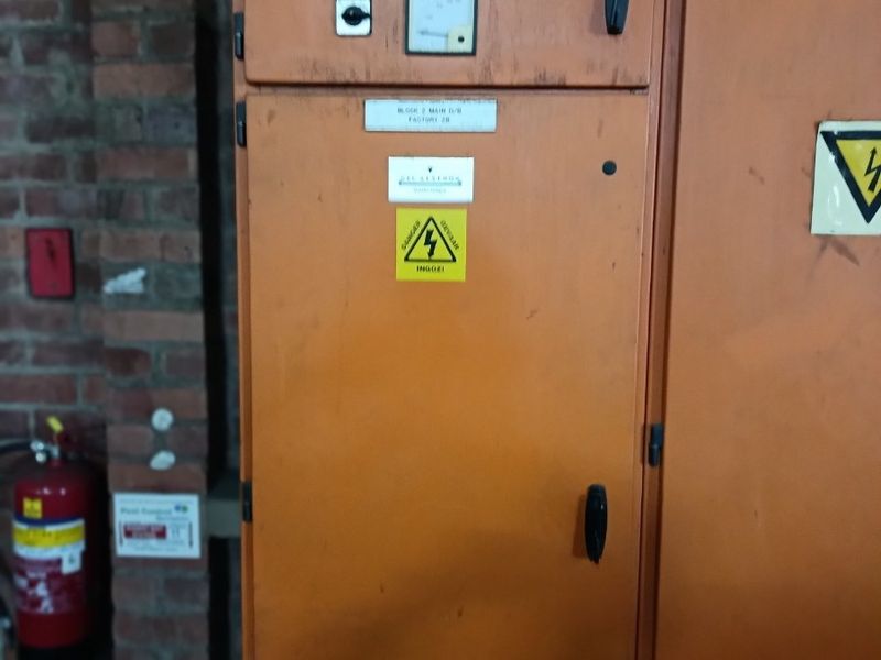 Industrial electrical distribution board mounted against an exposed brick wall in a utility area.