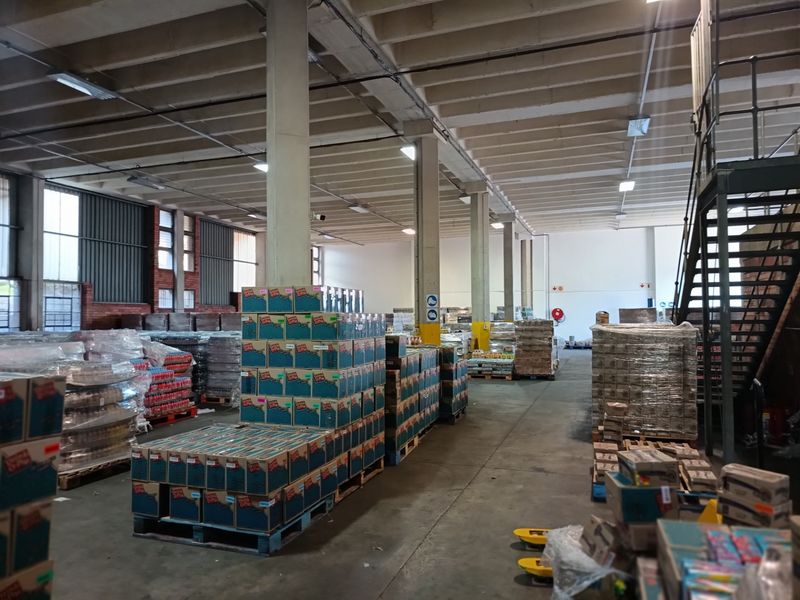 Spacious industrial warehouse area featuring high ceilings, concrete structural columns, and a metal staircase, currently utilized for storage and logistics.