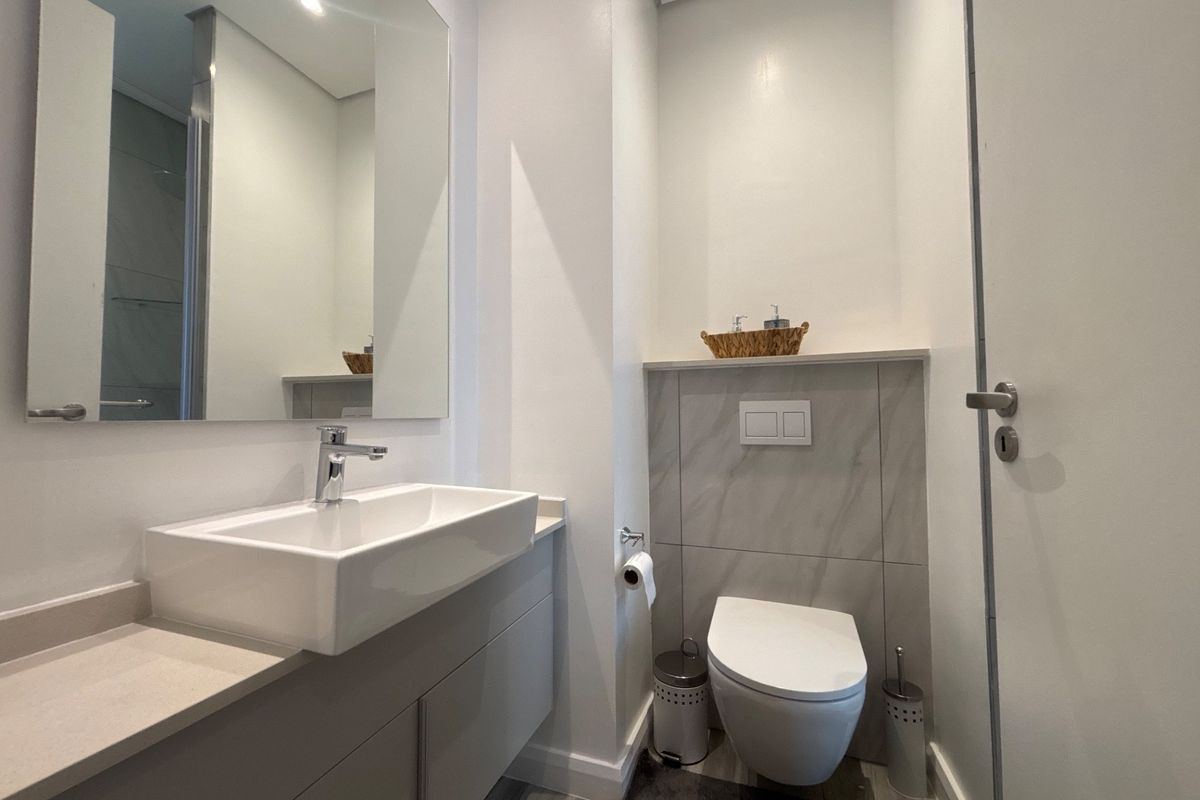 Modern bathroom featuring a wall-mounted toilet with concealed cistern, sleek vanity cabinet with basin, and a large wall mirror.