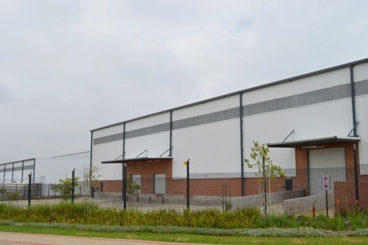 A modern industrial warehouse facility featuring corrugated metal cladding, brick accents, secure perimeter fencing, and multiple loading bay access points.