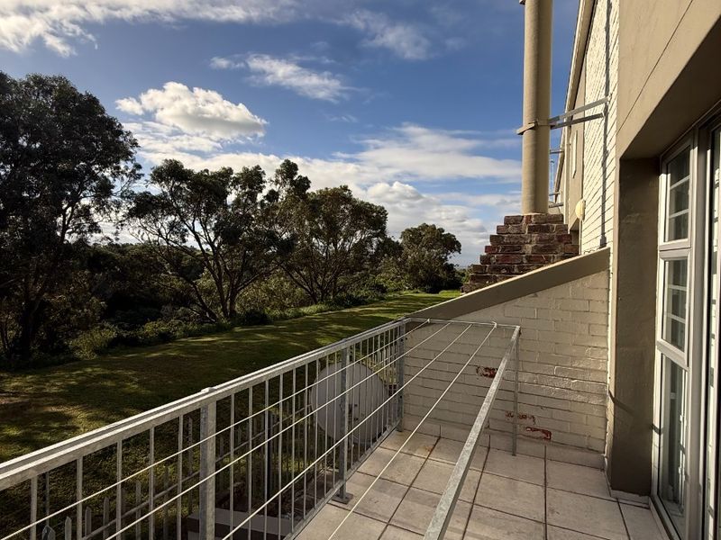A spacious balcony featuring tiled flooring, a metal balustrade, and an external chimney flue, overlooking a green landscape.
