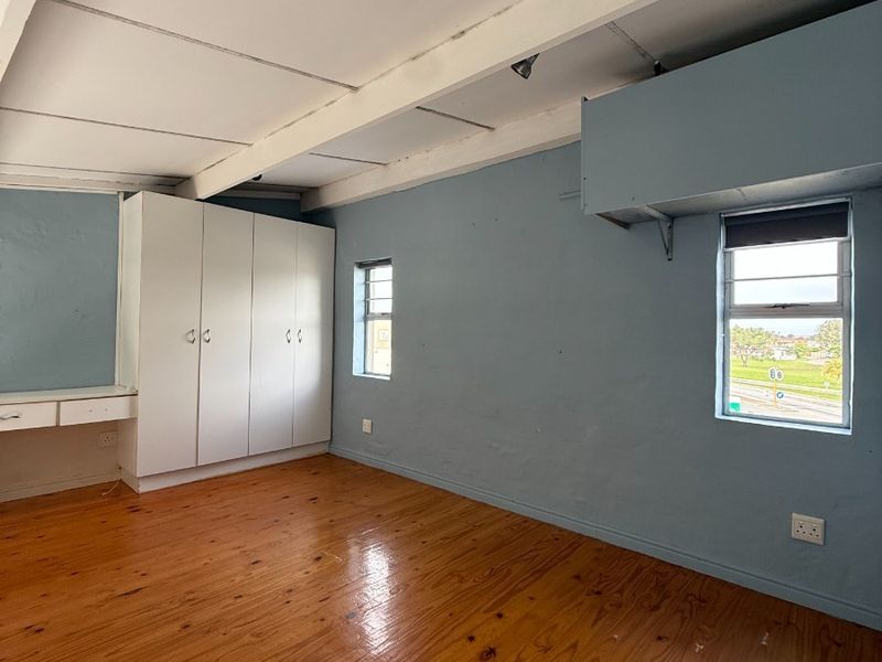 An empty bedroom featuring polished timber flooring, exposed ceiling beams, built-in wardrobe storage, and a integrated desk area with louver windows.