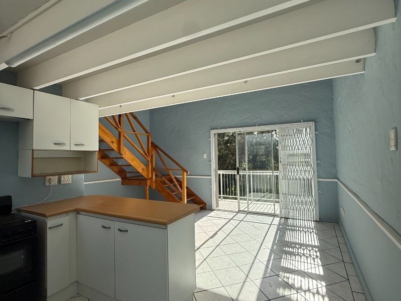 Open plan living area featuring a kitchen with laminate countertops, exposed ceiling beams, tiled flooring, and a staircase leading to an upper level.
