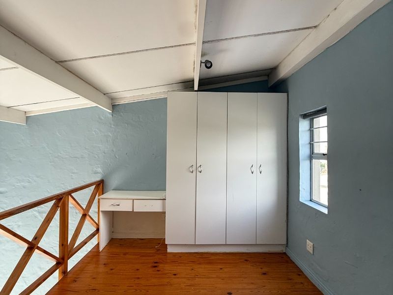 Loft-style bedroom featuring timber flooring, built-in wardrobe, integrated desk, and exposed beam ceiling. Requires maintenance to address ceiling water staining.