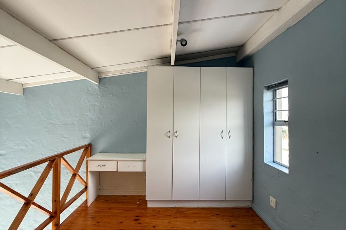 Loft-style bedroom featuring timber flooring, built-in wardrobe, integrated desk, and exposed beam ceiling. Requires maintenance to address ceiling water staining.