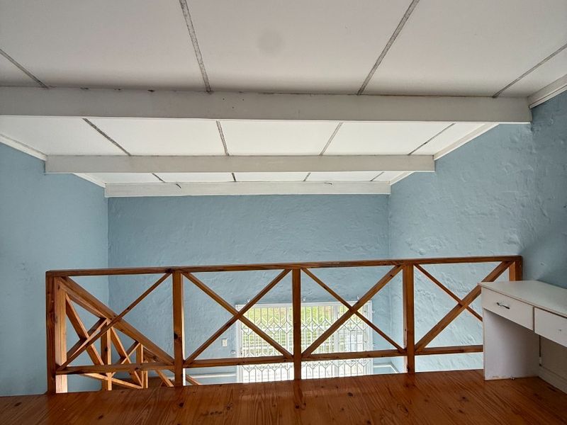An open loft-style bedroom area featuring polished wooden flooring, a wooden balustrade, and a suspended ceiling, overlooking the lower level through a security gate.