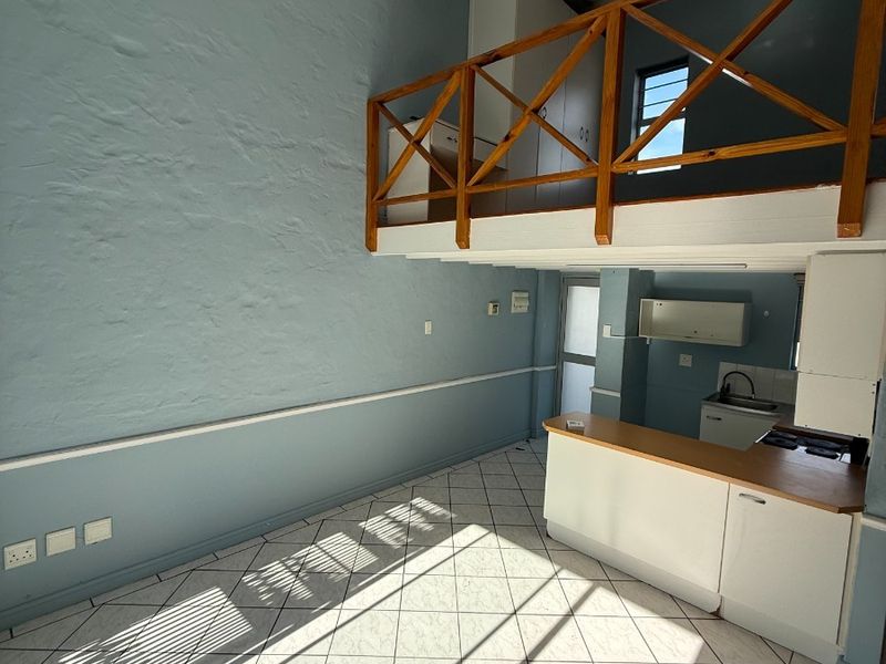 Open plan living area featuring a mezzanine level with wooden balustrade, tiled flooring, and a compact kitchen with built-in cabinetry and hob.