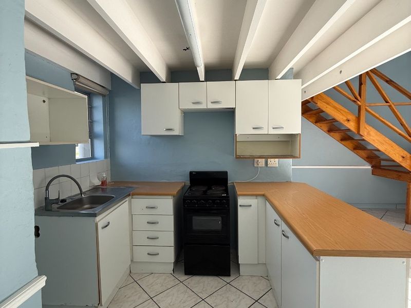 A functional kitchen featuring built-in cabinetry, laminate countertops, a stainless steel sink, and a freestanding stove, set against a backdrop of exposed ceiling beams.