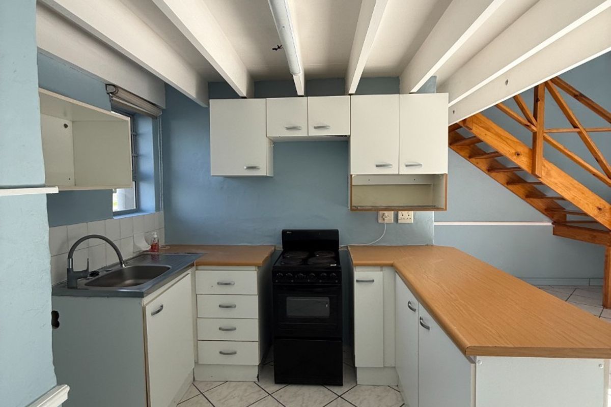 A functional kitchen featuring built-in cabinetry, laminate countertops, a stainless steel sink, and a freestanding stove, set against a backdrop of exposed ceiling beams.