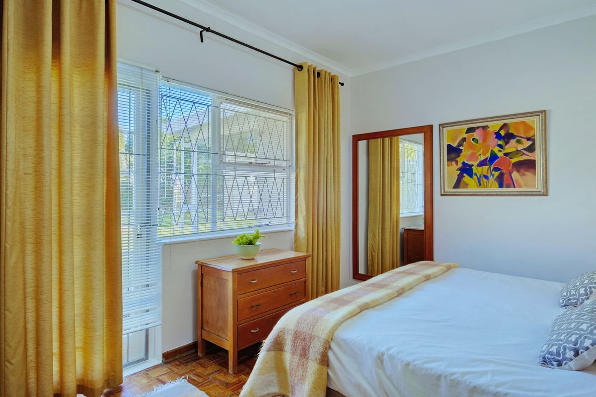 A well-lit bedroom featuring classic parquet flooring and a window fitted with security bars, offering a clean and functional living space.