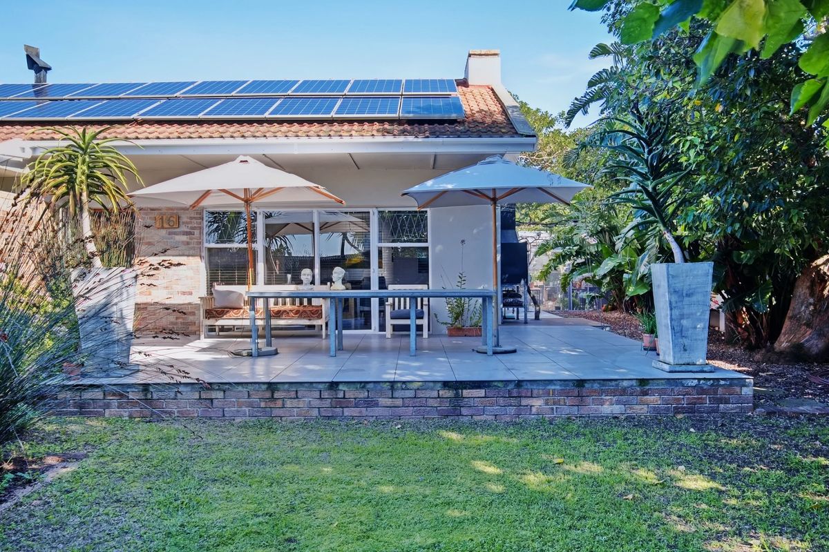 Rear view of the property featuring a tiled patio, built-in braai, sliding door access, and roof-mounted solar panels overlooking a garden.