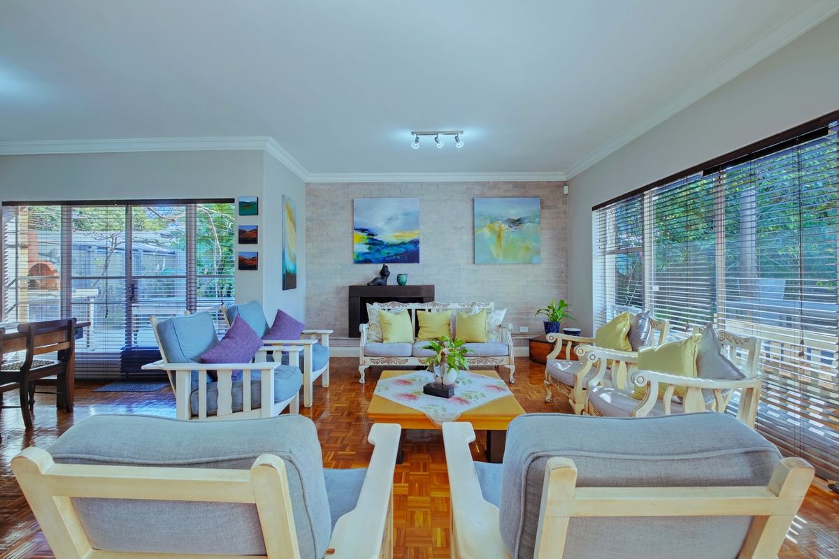 A spacious living room featuring classic parquet flooring, a textured brick feature wall with a fireplace, and large windows with venetian blinds.