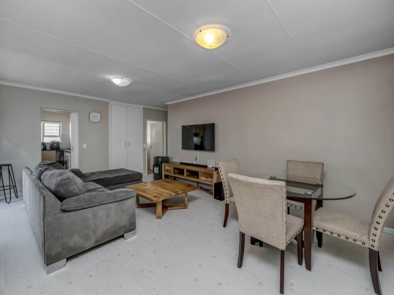 An open-plan living and dining area featuring neutral wall tones, laminate flooring, and built-in storage cupboards, with a clear view into the adjacent kitchen space.
