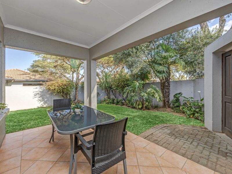 A covered patio area featuring tiled flooring, overlooking a private garden with established landscaping and boundary walls.