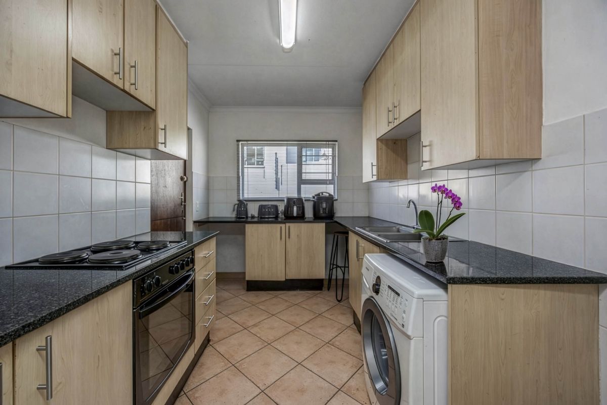 A functional galley-style kitchen featuring light wood cabinetry, dark granite countertops, tiled backsplash, and integrated laundry plumbing.