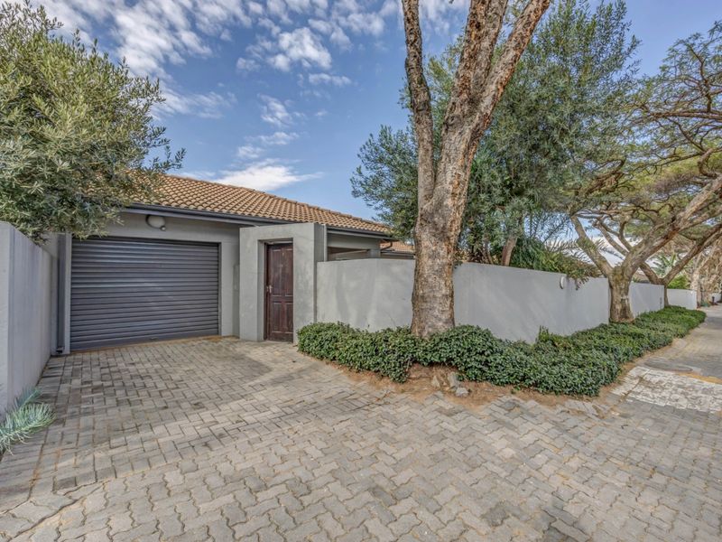 Front exterior view of the property featuring a paved driveway, a secure roller garage door, and a private entrance gate with established boundary walls.