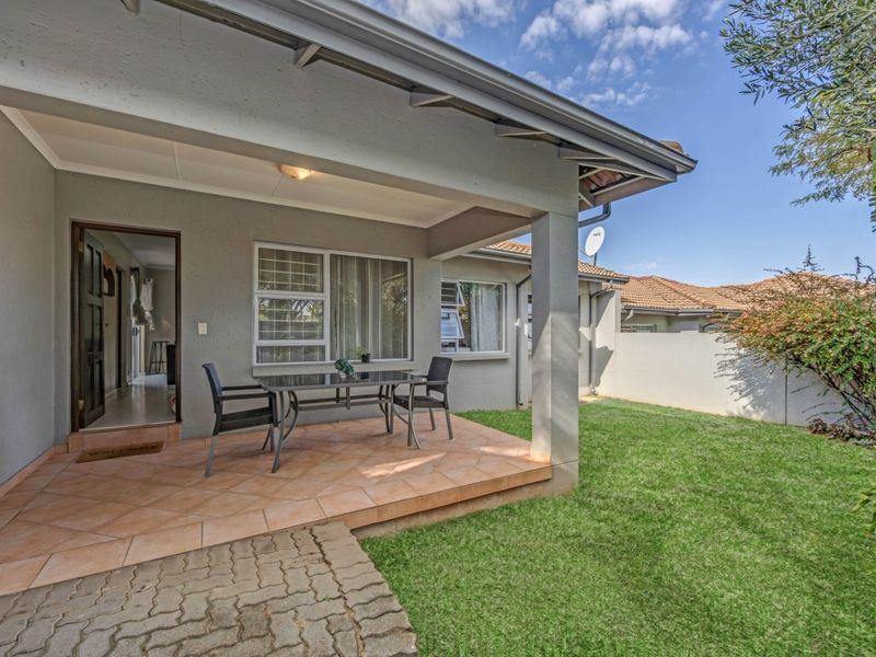 A covered patio area featuring tiled flooring, overlooking a private garden with a brick paved walkway and boundary wall.