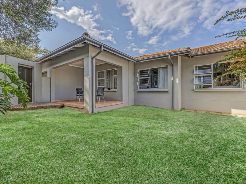 Rear view of the house featuring a covered patio area, tiled flooring, and well-maintained lawn with established garden surroundings.