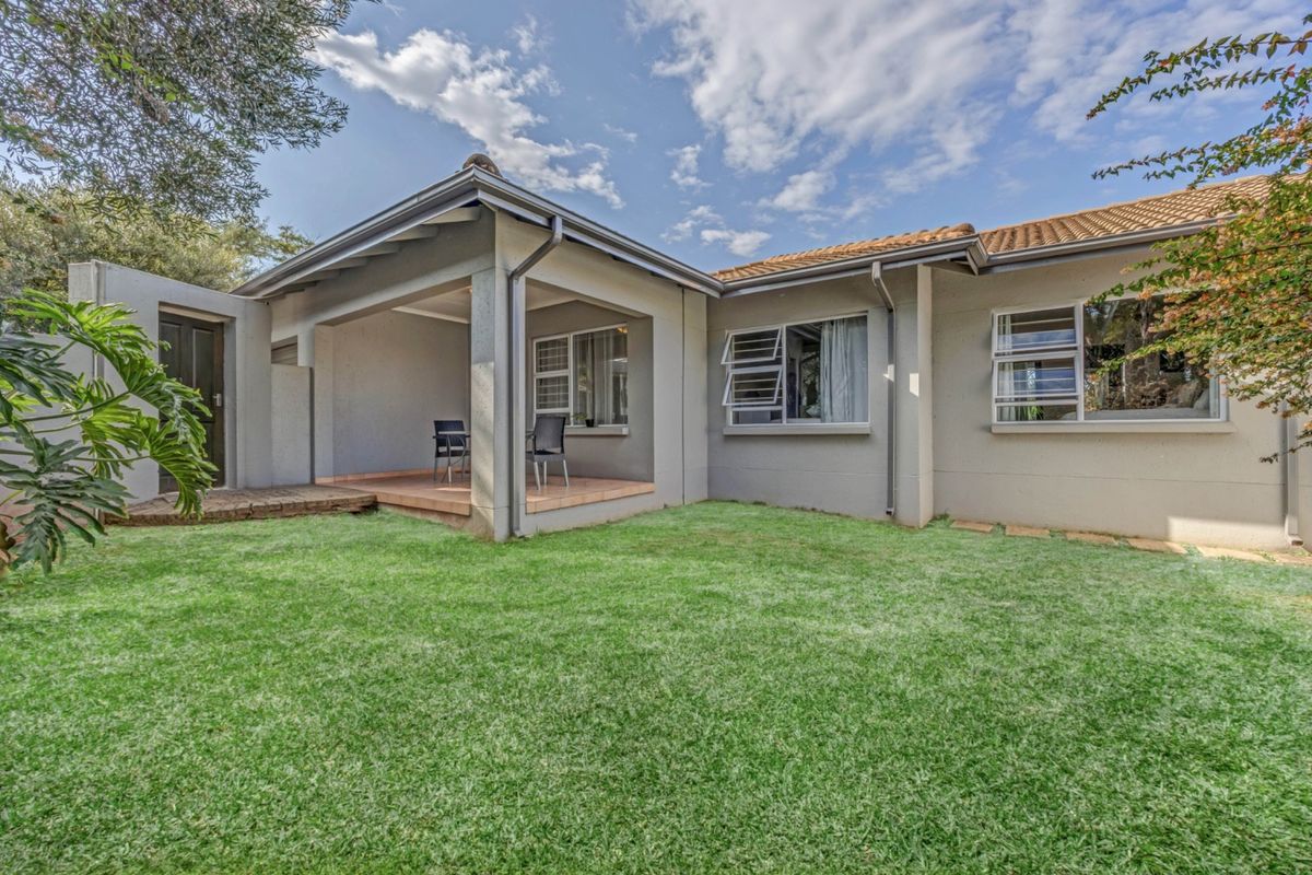 Rear view of the house featuring a covered patio area, tiled flooring, and well-maintained lawn with established garden surroundings.